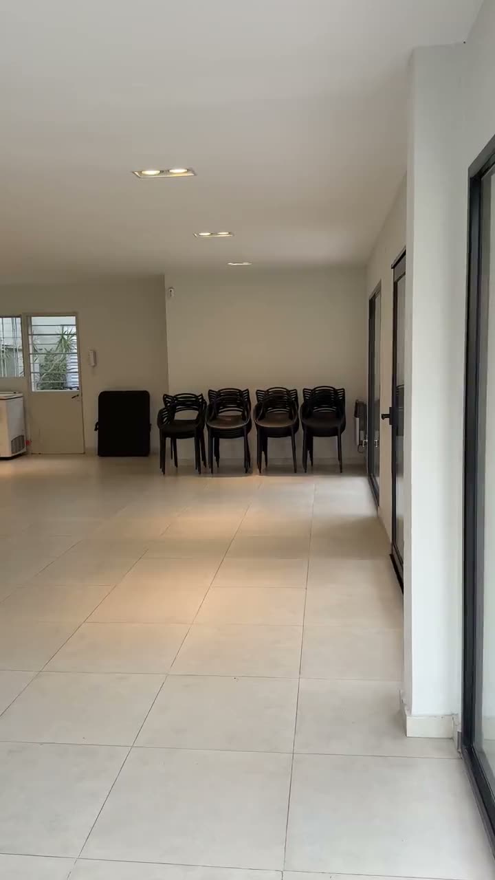 El salón de punta a punta, con el piso claro, las sillas al fondo y el ventanal a un costado